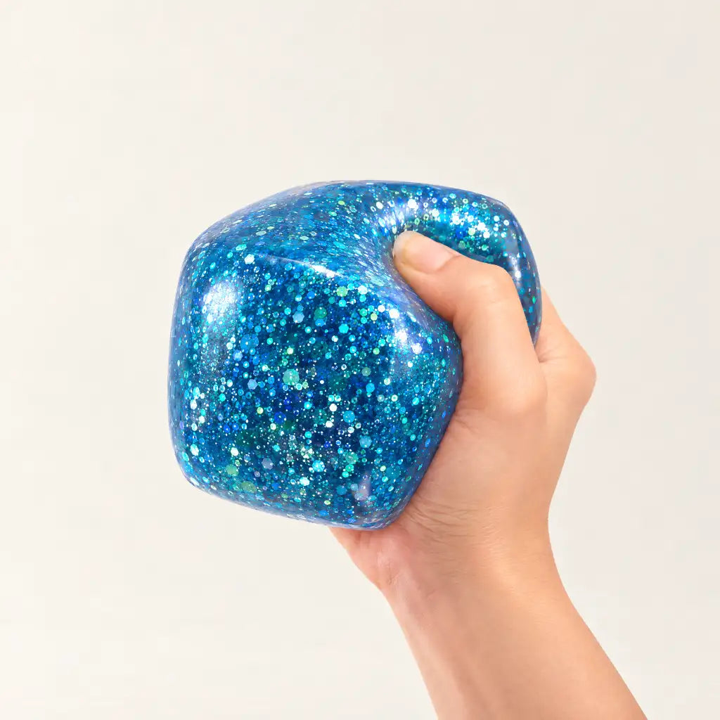 Blue Discovery Zone Jumbo Sparkly Squish Cube being squeezed in one hand.