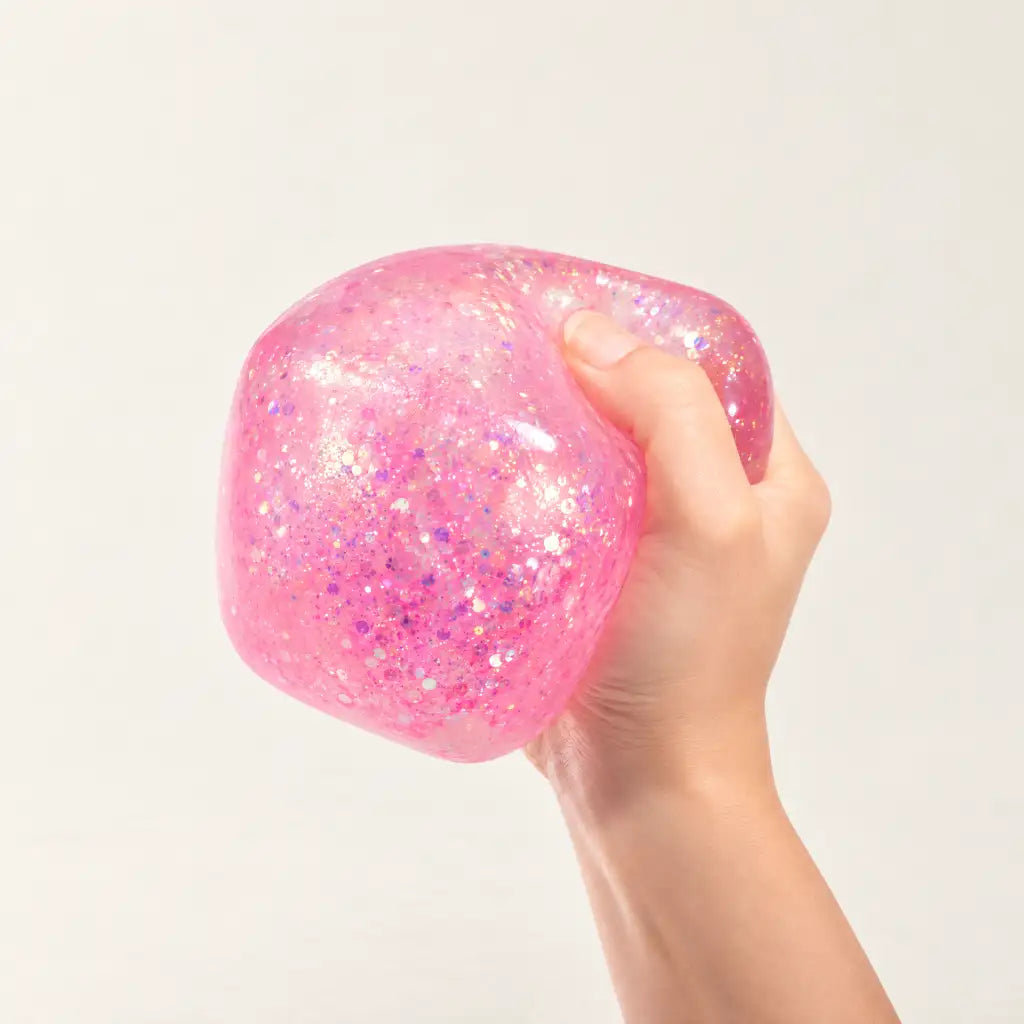 Pink Discovery Zone Jumbo Sparkly Squish Cube being squeezed in one hand.